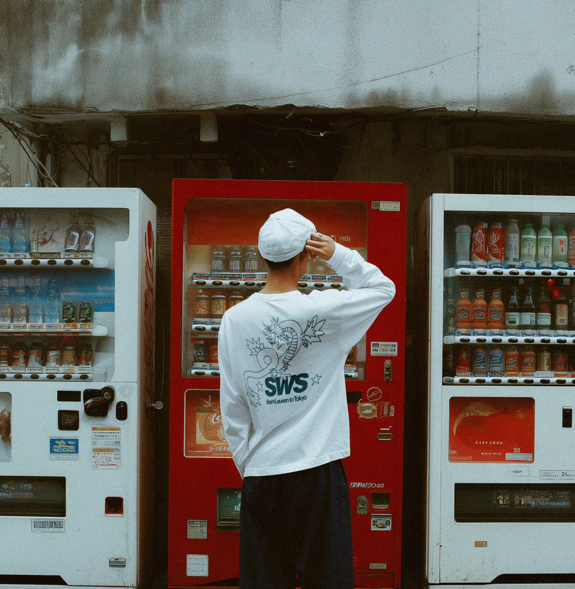 Person wearing a white sweatshirt with 'SWS' logo in front of red and white vending machines.